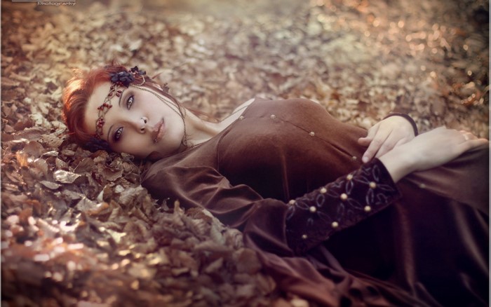 Woman with red hair lying in autumn leaves