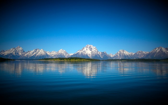 Snow-capped mountains reflected in a lake under a clear blue sky