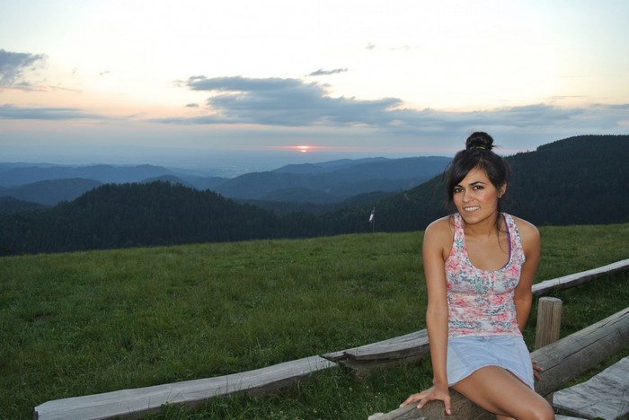 Woman sitting on a wooden fence overlooking mountains at sunset