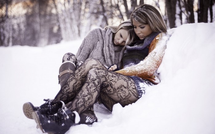 Two women in winter fashion sitting in the snow