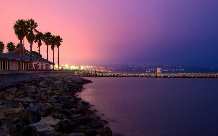 Coastal restaurant and harbor at sunset with city lights