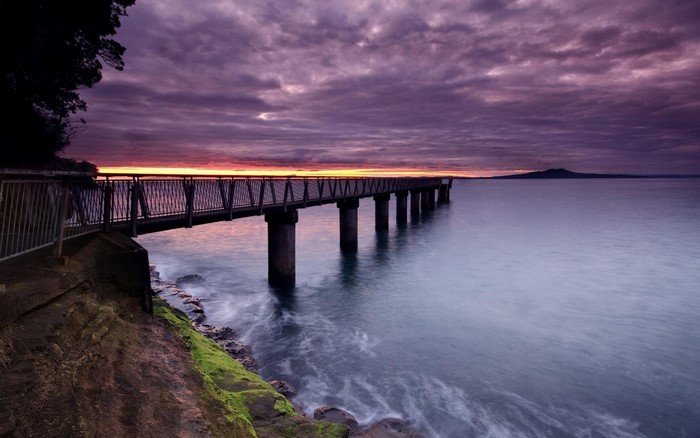 Pier over the sea at sunset with Mount Rangitoto in the distance