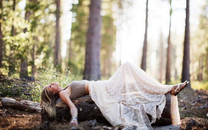 Woman in lace dress lying on a log in a forest