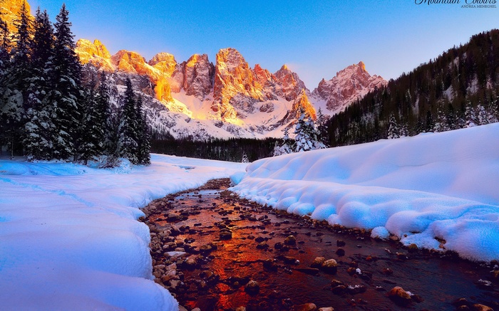 Snowy mountain landscape with stream and pine trees