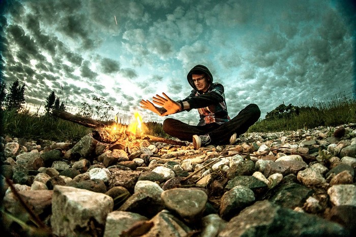 Man warming hands by campfire under cloudy sky