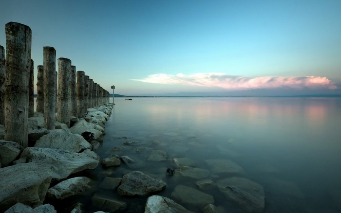 Wooden posts and rocks on a calm lake at dusk