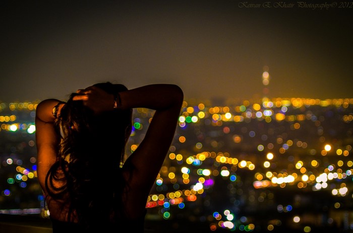 Woman with hands on head overlooking city lights at night