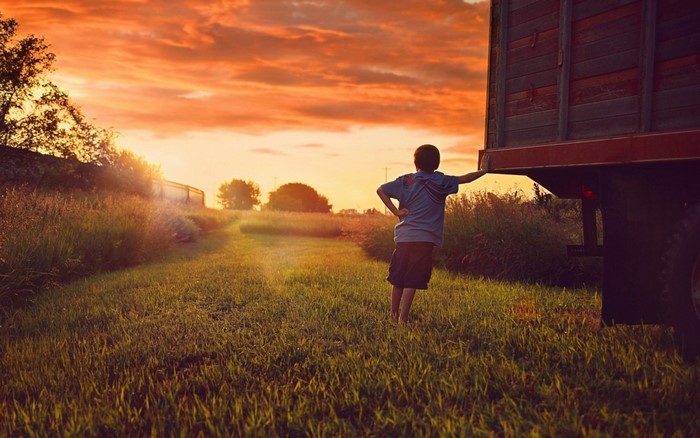 Boy leaning on truck at sunset in a field