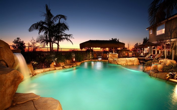 Luxury swimming pool at dusk with waterfall and tiki bar
