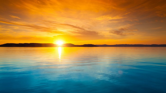 Sunset over the ocean with a mountain range on the horizon