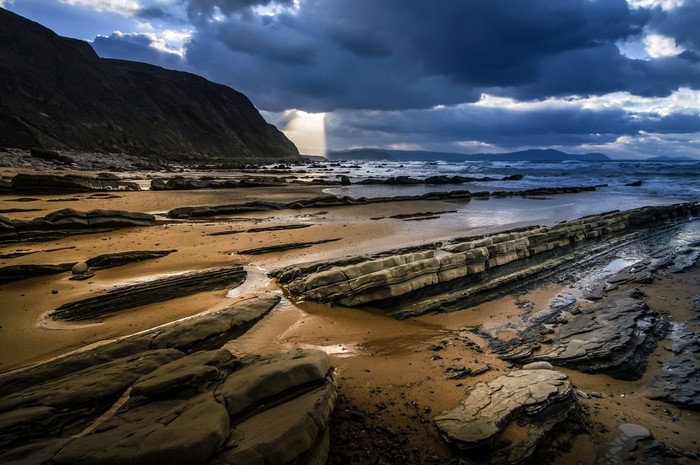Rocky beach with dramatic clouds and sunlight breaking through