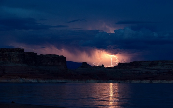 Lightning strikes over a desert landscape and lake at dusk
