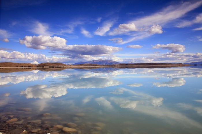 Calm lake reflecting clouds and mountains under a blue sky