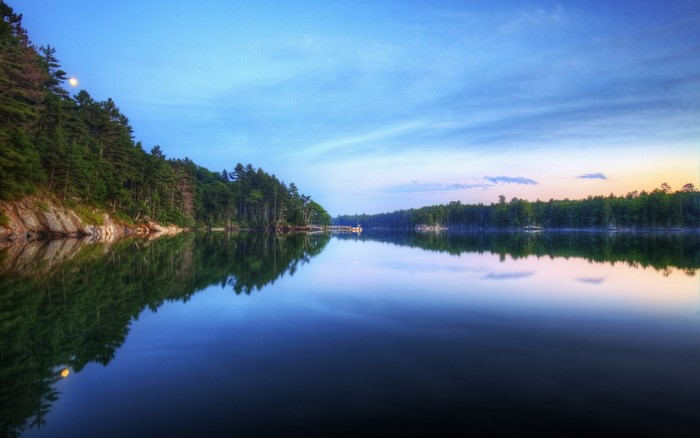 Calm lake reflecting trees and sky at dawn