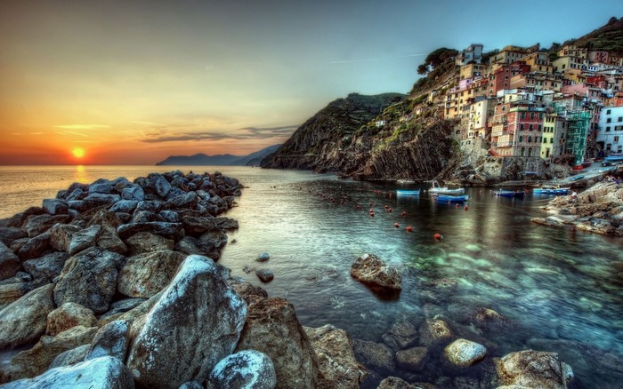 Sunset over a rocky coast with colorful buildings on a cliffside