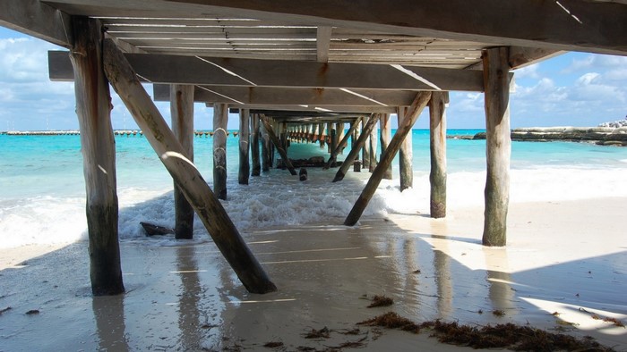 Under a wooden pier on a tropical beach with turquoise water