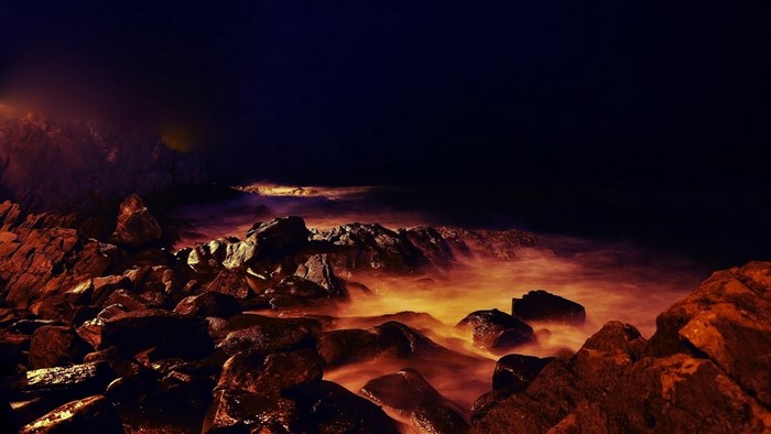 Rocky coastline at night with glowing water