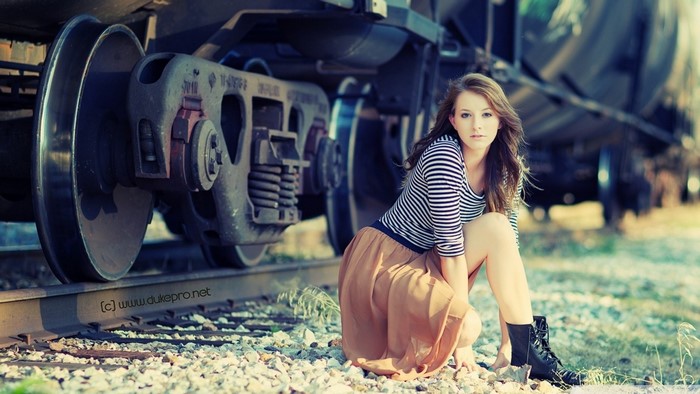 Woman posing by a train on railroad tracks