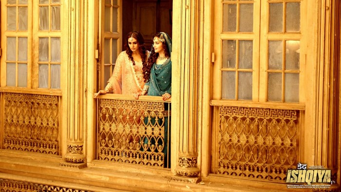 Two women in traditional Indian attire looking out of a wooden balcony