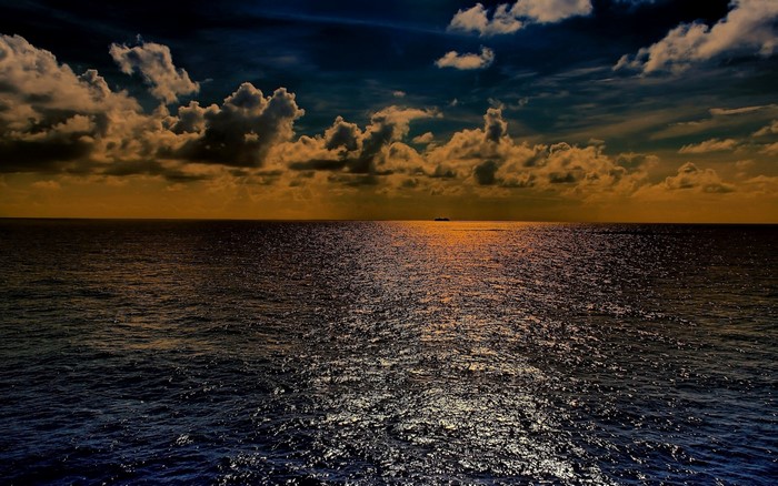 Sunset over the ocean with clouds and a distant ship