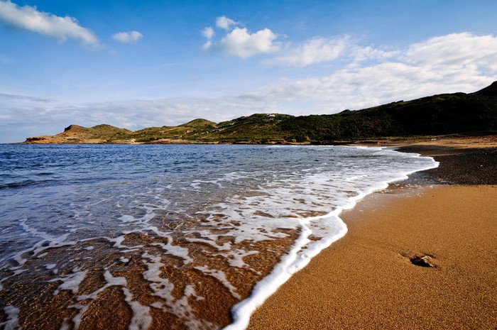Sandy beach with waves and hills under a blue sky