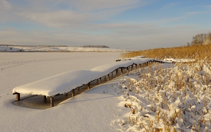 Snow-covered wooden pier on a frozen lake in winter
