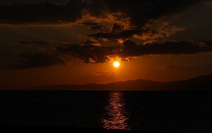 Sunset over the sea with clouds and mountains