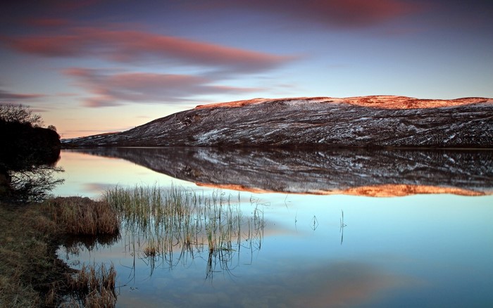 Snow-capped hill reflected in calm lake at sunset
