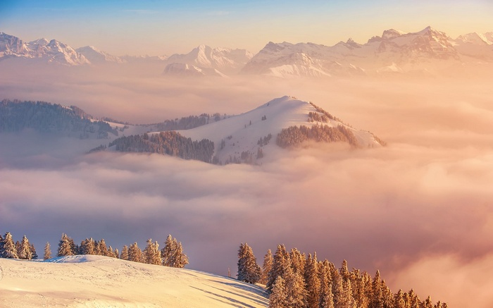 Snowy mountain peaks above clouds at sunrise
