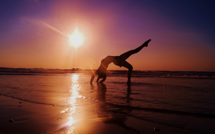 Woman doing a backbend on a beach at sunset