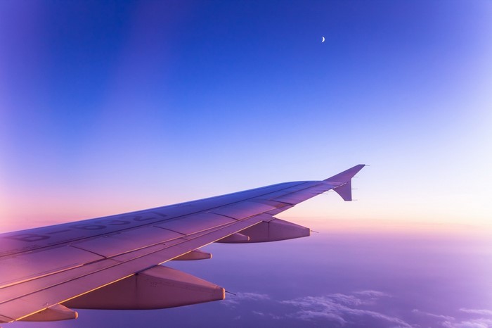 Airplane wing flying through the sky at sunset with moon