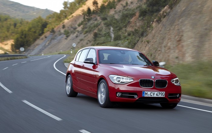 Red BMW 1 Series driving on a winding road
