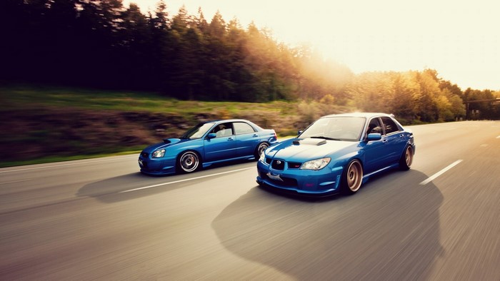 Two blue Subaru Impreza WRX STi cars driving on a road