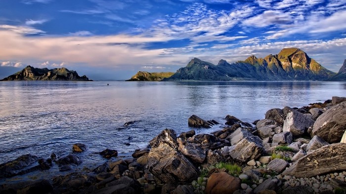 Rocky shore with mountains and sea under cloudy sky