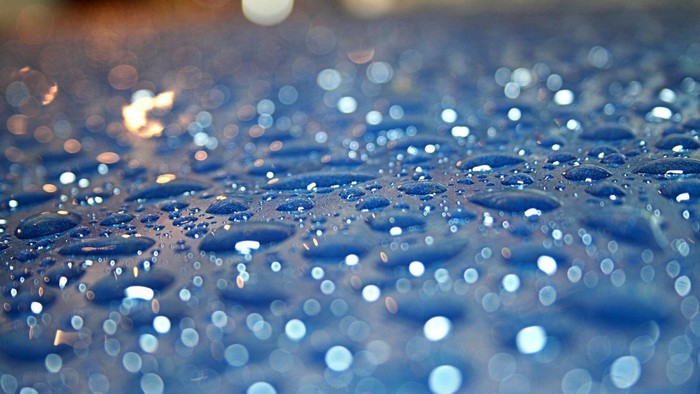 Close-up of water drops on a blue surface with bokeh