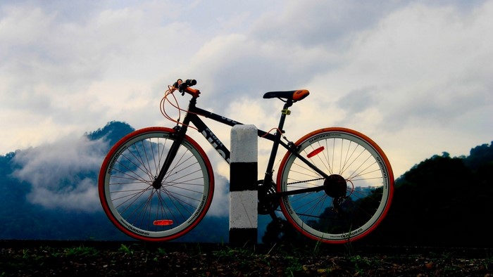 Bicycle leaning on a post with mountains and clouds