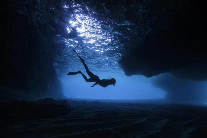 Woman free diving in a dark underwater cave