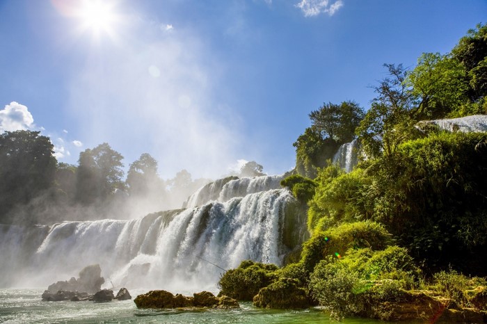 Sunlight over a cascading waterfall surrounded by trees