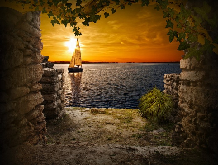 Sailboat on the sea at sunset through stone archway