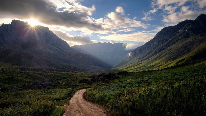 Sunlight streams through a mountain valley with a dirt road