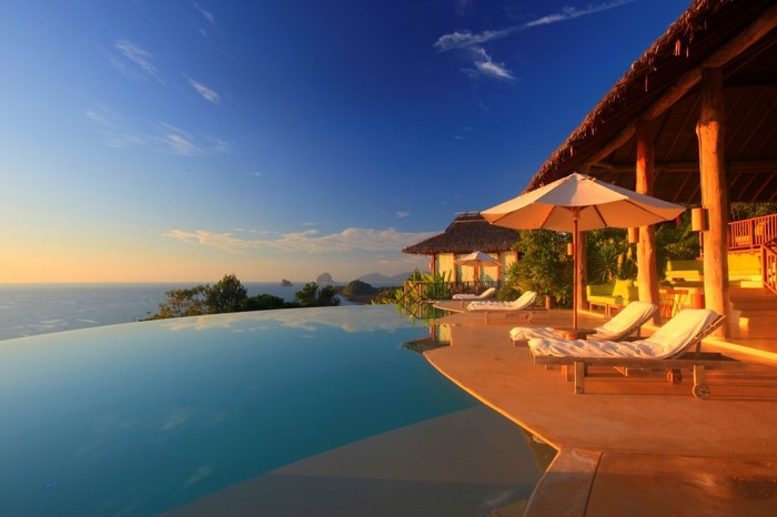 Infinity pool overlooking the ocean at sunset with lounge chairs