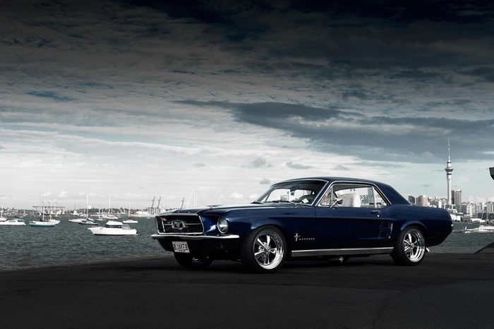 Blue 1967 Ford Mustang parked by the water with city skyline