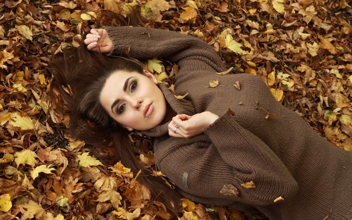 Woman lying in autumn leaves wearing a brown sweater