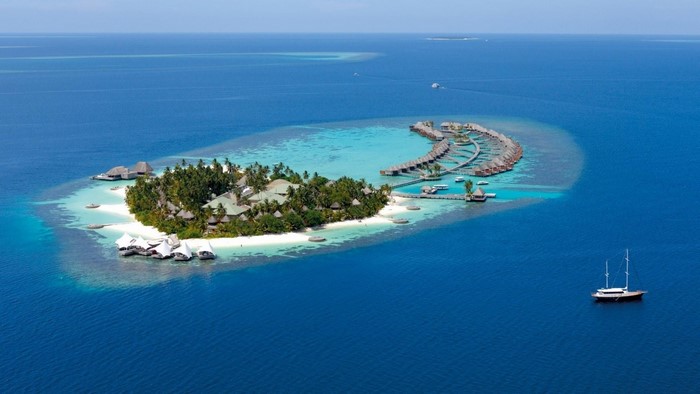 Aerial view of a tropical island resort with overwater bungalows and a sailboat