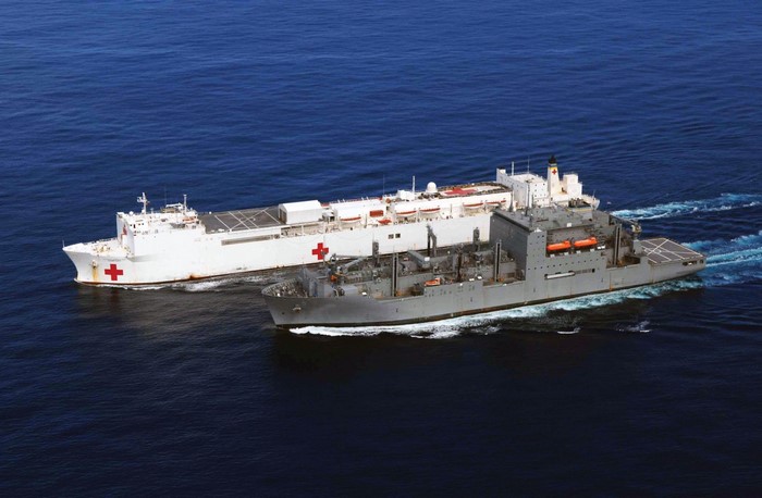 Two ships sailing on the sea, one white with red cross, one gray
