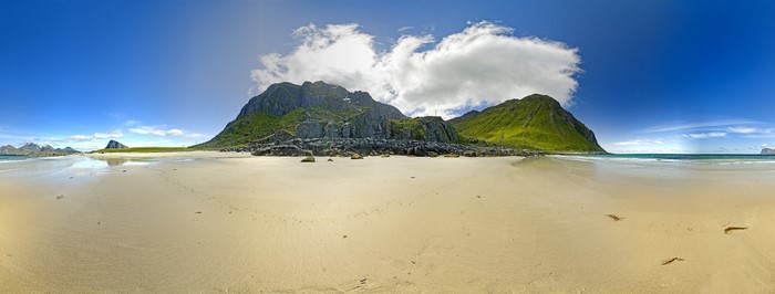 Panoramic view of a sandy beach with green mountains and blue sky