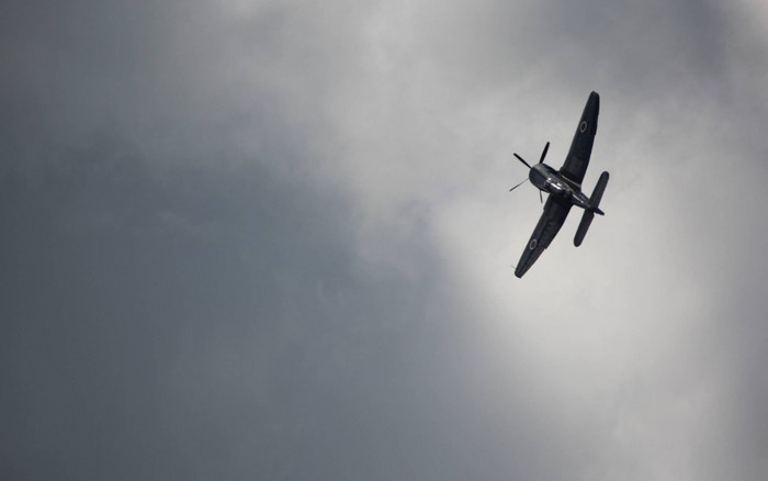 Dark airplane with propeller flying in cloudy sky
