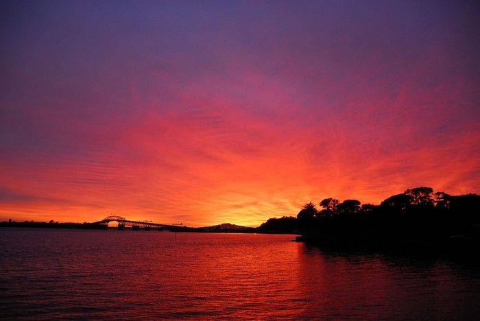 Sunset over water with bridge and trees