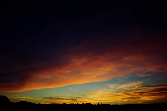 Sunset sky with orange and blue clouds over silhouette of hills