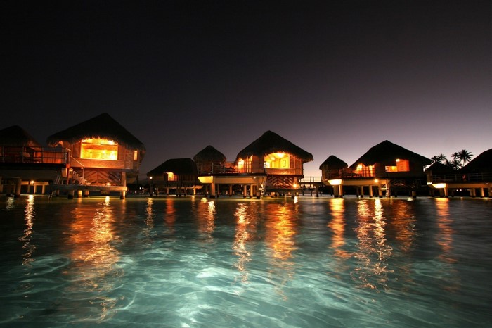 Overwater bungalows at night with reflections in the water